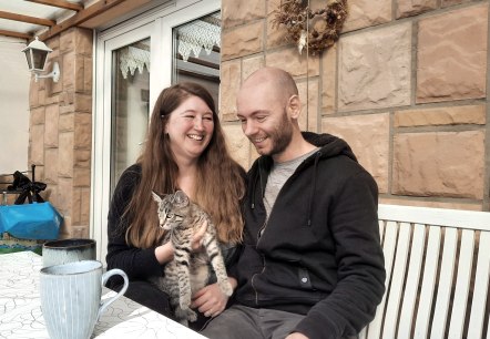 Julia und Helge mit Katze auf dem sonnigen Balkon, © Zukunftsinitiative Eifel