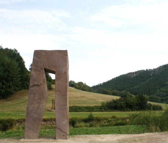 „Brückenschlag“ heißen die zwei Arbeiten von Christoph Mancke aus Lünebach. Er platzierte den offenen Sandsteinblock, ein stilisierter schreitender Mensch und seine stählerne Verdoppelung, dies- und jenseits des Grenzflusses Our. Der Durchblick schafft die Verbindung., © Eifel hautnah, Stefan Lieser